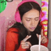 a woman wearing pink headphones and a red shirt is holding a cup of milkshake with a straw .