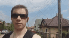 a man wearing sunglasses and earbuds stands in front of a row of houses