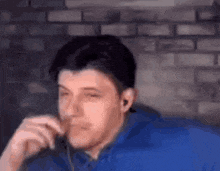 a man in a blue shirt is sitting in front of a brick wall .