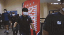 a group of people wearing face masks are walking in front of a sign that says persib tv