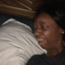 a woman is smiling while laying in bed with a pillow .