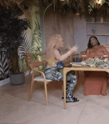 two women are sitting at a table and one of them is wearing a shirt that says ' a ' on it