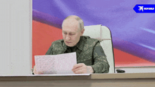 a man in a military uniform sits at a desk reading a paper
