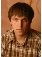 a man in a plaid shirt looks at the camera with a serious look on his face