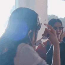 a woman wearing sunglasses is looking at herself in a mirror while another woman looks on .