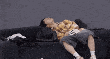 a person laying on a black couch with their head on a pillow