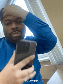 a man in a blue shirt is holding a cell phone with face app written on it