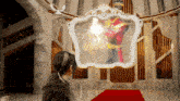 a woman stands in front of a mirror that shows a man in a red suit