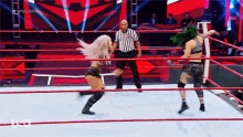 two women are wrestling in a wrestling ring with a referee in the background .