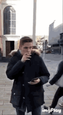 a man in a parka is smoking a cigarette while walking down a sidewalk .