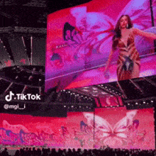 a woman is dancing in front of a large screen that says tiktok on it