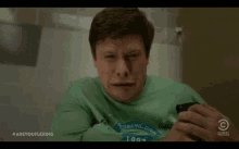 a man in a green shirt is crying while holding a cell phone in a bathroom stall .