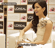 a woman in a white dress is sitting in front of a wall with l' oreal advertisements .