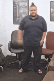 a man in a blue shirt and black pants stands in front of an office chair