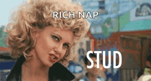 a woman with blonde curly hair is standing in front of a building with the words `` rich nap stud '' written above her .