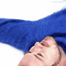 a man wearing a blue furry sweater is laying down on his back with his eyes closed .
