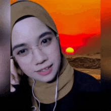 a woman wearing glasses and a hijab is smiling in front of a sunset