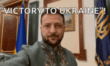 a man with a beard is standing in front of flags and says " victory to ukraine "