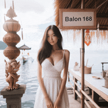 a woman in a white dress is standing in front of a sign that says balon 168