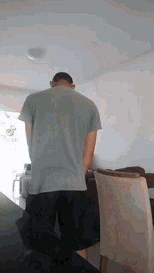 a man in a grey shirt and black shorts stands in a living room with his head down