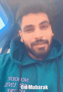 a man with a beard is wearing a blue hoodie that says eid mubarak