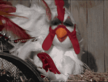 a stuffed chicken with a red beak is sitting on a pile of hay