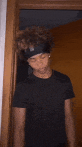 a young man wearing a headband and a black shirt is standing in front of a doorway .