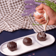 a white plate with three chocolates on it and a hand squeezing whipped cream