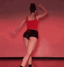 a woman in a red tank top and black shorts is dancing on a stage .