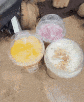 three plastic cups of different flavors are on the floor