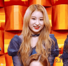 a woman with long blonde hair is smiling in front of a wall that has the word buzz on it