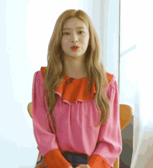 a woman is sitting in a chair wearing a pink blouse with red sleeves .