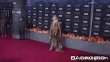 a woman stands on a red carpet in front of a wall that has got written on it