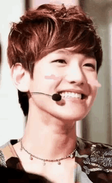 a young man wearing a necklace and a microphone on his face is smiling .