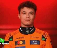 a man wearing an orange racing suit with logos for android and cisco