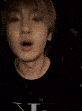 a close up of a young man with his mouth open wearing a black shirt and a necklace .