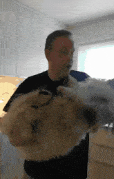 a man in a black shirt is holding a white dog in his arms