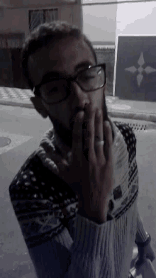 a man wearing glasses and a sweater is covering his mouth with his hand