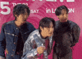 a group of young men are standing in front of a pink sign that says 5th sat in london