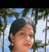 a woman with a red bindi on her forehead is standing in front of palm trees .