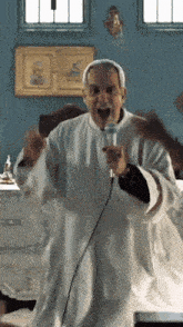 a man in a white robe is singing into a microphone in a room