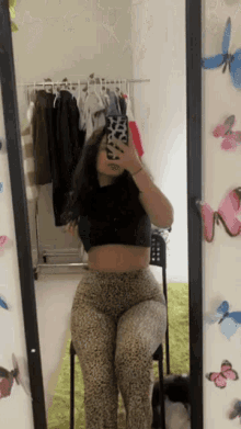 a woman is taking a selfie in front of a mirror with butterflies on the wall behind her .
