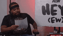 a man reading a piece of paper in front of a sign that says hey ( ew )
