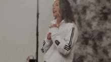 a woman wearing a white adidas sweatshirt is standing in front of a wall