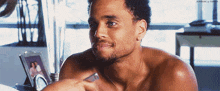 a shirtless man is sitting in front of a window and holding a remote control
