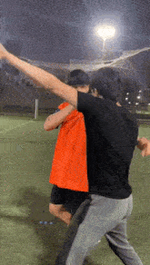 a man in an orange shirt is standing next to another man in a black shirt .