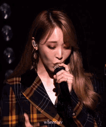 a woman in a plaid jacket is singing into a microphone with the words wheelluv below her