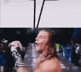 a man without a shirt is standing in front of a crowd while a drawing of a man is behind him .