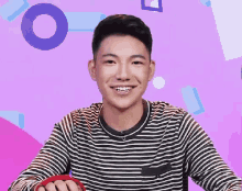 a young man wearing a striped shirt is smiling and holding a red object .