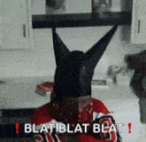 a man wearing a black hat with horns and a bandana on his face is sitting in a kitchen .